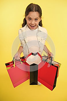 Check out her profitable purchases. Girl carries shopping bags yellow background. Girl fond of shopping. Child cute