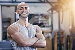 Check out those muscles on full display. Portrait of a muscular young man standing with his arms crossed in a gym.