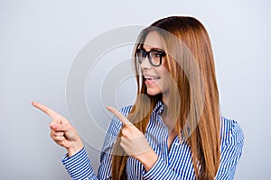 Check this out! Smiling cute lady is pointing on the copy space, wearing smart striped shirt, standing on pure blue background is