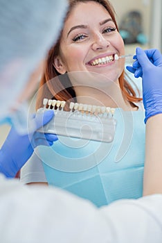 Check and select the color of the teeth in the dentist chair. Dentist makes the process of treating a beautiful young red-haired