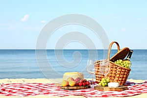 Checkered blanket with picnic basket and products on beach. Space for text