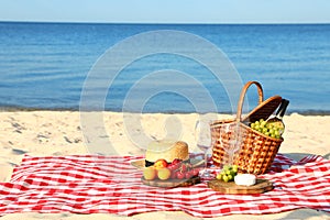 Checkered blanket with picnic basket and products on sunny beach