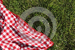 Checkered picnic tablecloth on fresh green grass, top view. Space for text