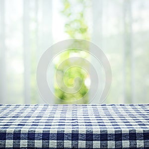 Checkered tablecloth texture top on blur of curtain with window view green from tree garden background