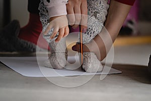 Checking baby foot size mother holding leg of her child on the blank paper drawing around with pencil to measure feet size family