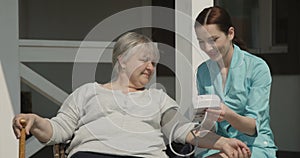 Checking Blood Pressure to Elderly Woman Nurse is Smiling and Caring for Old People Outdoors on Sunny Day at the Nursing Home shot