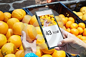 Checking calories on orange fruit in store with smartphone