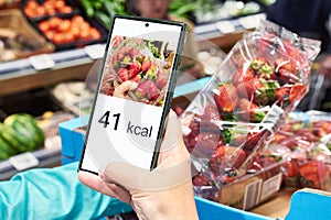 Checking calories on strawberry in store with smartphone