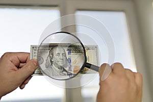 Checking counterfeit money light. 100 dollars against the window in his hand. Check for watermark on new hundred dollar