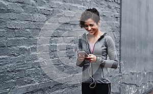 Checking my text messages before running. an attractive young woman wearing earphones and using her cellphone while