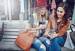 Checking for sales online. two young girlfriends sending text messages while sitting on a bench during a shopping spree.