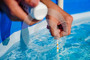 Checking the water quality of a pool with the help of a test strip with PH value, chlorine and algaecide