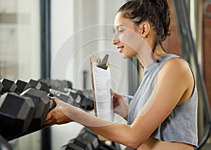 Checklist, exercise and inspection with personal trainer woman checking equipment or weights in gym. Dumbbell, fitness