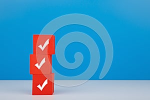 Checkmarks on three red blocks on white table against blue background with copy space