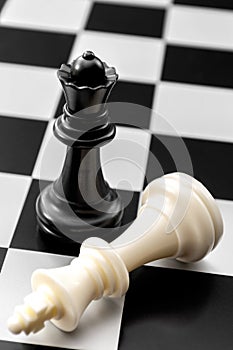 Checkmate, gender issues and fall of powerful leader concept with fallen white king and standing black queen on chess board