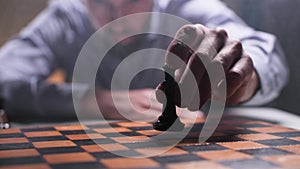 Checkmate, pensive man plays chess and puts a chess piece on a chessboard, close-up