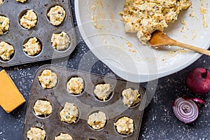 Cheddar cheese and herbs mini muffin dough uncooked being placed in muffin baking trays