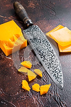Cheddar Cheese sliced on a kitchen table with knife. dark background. Top view