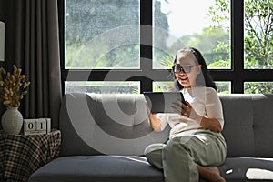 Cheedul middle age woman in casual clothes browsing internet on digital tablet at home