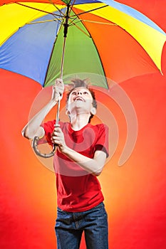 Cheeful funny boy in red t-shirt holding a multicolored umbrella