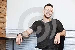 Cheeful guy in black tshirt sitting at bright modern room.