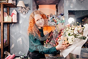 Cheeful young florist standing next to bouquets of vernal flowers in shop