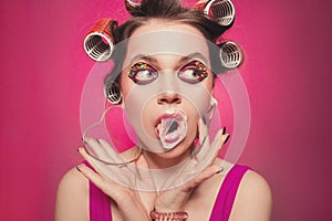 Cheeky girl with bubble gum posing on pink background in body, with curlers on head. Pretty woman with sweet makeup making