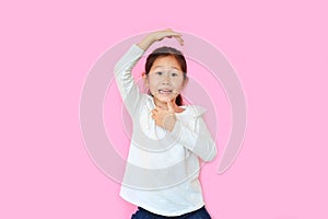 Cheeky little asian kid girl with expression monkey face and hands isolated on pink background. Amusing playful child monkeying