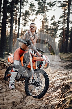 Female racer wearing motocross outfit with semi naked torso sitting on her bike in the forest