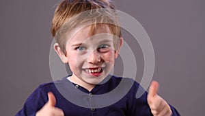 Cheeky young preschool red hair boy with freckles showing his excitement with double thumbs up, grey background studio