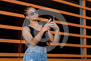 Cheerfu Afro-American lady with deadlocks using her phone in front of an orange construction