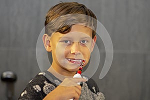 A cheerful 10-year-old boy is brushing his teeth with an electric toothbrush in the bathroom.