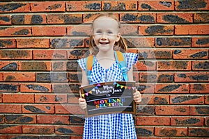 Cheerful 4 years old girl holding a poster with text `My first day in kindergarten` written in French