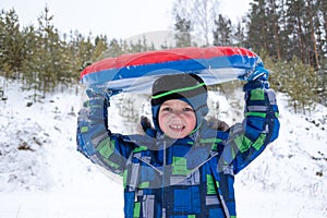 Cheerful active boy holding a winter inflatable tubing over his head outdoors. Cute little happy child having fun