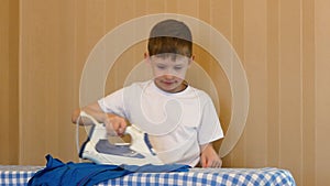 A cheerful, active Caucasian boy helps around the house and ironing clothes with an electric iron. The child helps with homework.