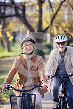 Cheerful active senior couple with bicycle in public park together having fun. Perfect activities for elderly people. Happy mature