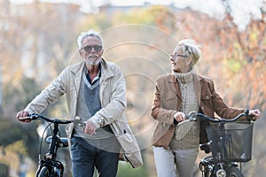 Cheerful active senior couple with bicycle in public park together having fun. Perfect activities for elderly people. Happy mature