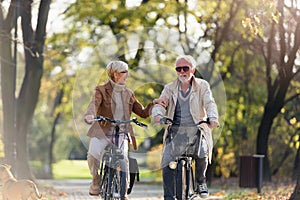 Cheerful active senior couple with bicycle in public park together having fun. Perfect activities for elderly people. Happy mature