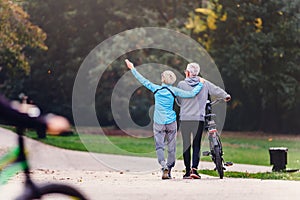 Cheerful active senior couple with bicycle walking in the park