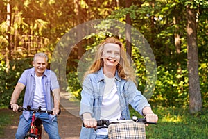 Cheerful active senior couple with bicycle walking through park together.