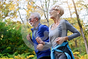 Cheerful active senior couple jogging in the park