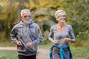 Cheerful active senior couple jogging in the park