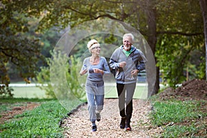 Cheerful active senior couple jogging in the park