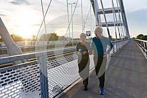 Cheerful active senior couple jogging together outdoors along the river