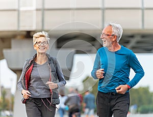 Cheerful active senior couple jogging together outdoors along the river