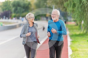 Cheerful active senior couple jogging together outdoors along the river