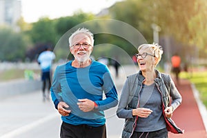 Cheerful active senior couple jogging together outdoors along the river