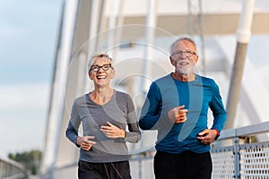 Cheerful active senior couple jogging together outdoors over the bridge