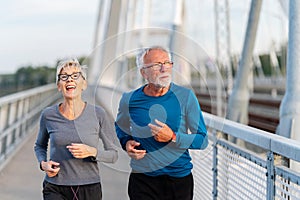 Cheerful active senior couple jogging together outdoors over the bridge