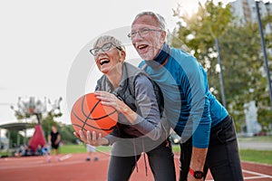 Cheerful active senior couple playing basketball on the urban basketball street court